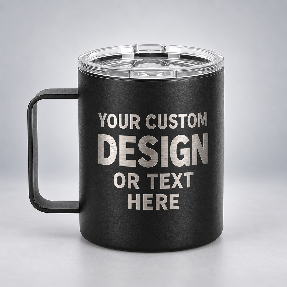 Illustrative black 12 oz handled coffee mug with silver YOUR CUSTOM DESIGN OR TEXT HERE engraving on a gray studio background