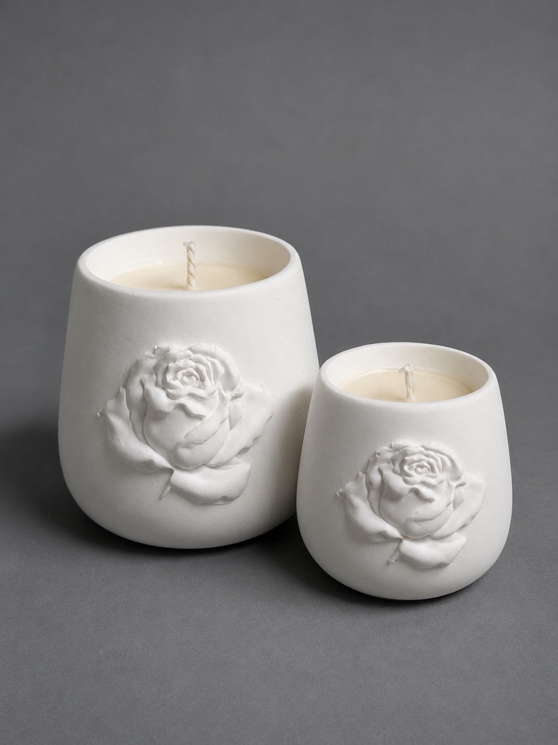 Two ivory candle vessels with raised rose details in 12 oz and 9 oz sizes