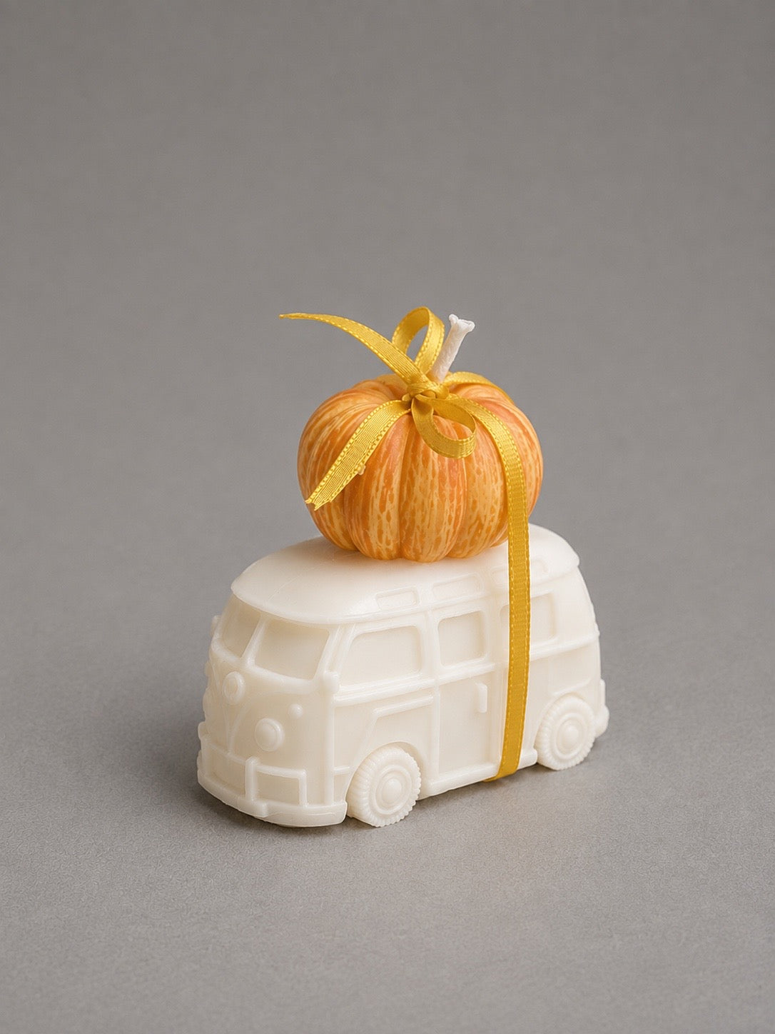 Small orange pumpkin candle with a golden bow resting on an ivory vintage van candle
