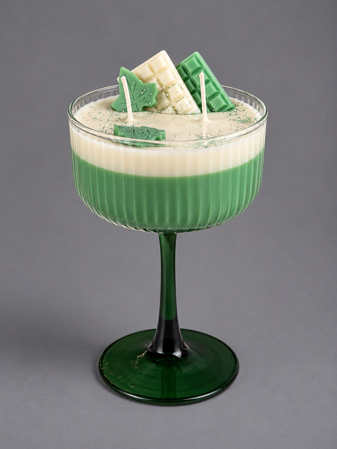 Two-wick matcha cocktail candle in a green stemmed glass with decorative wax pieces