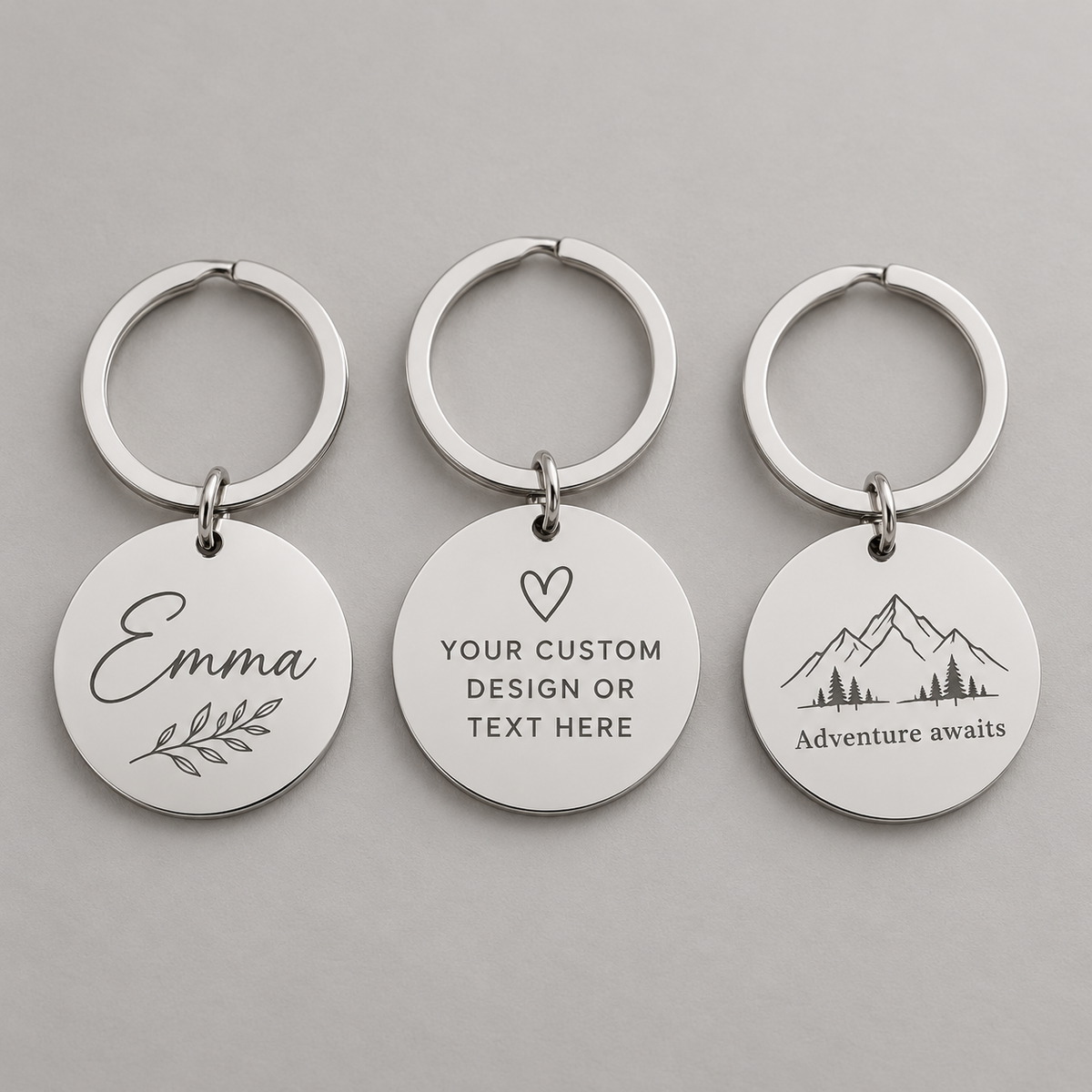 Digital mockup of silver round keychains showing custom name, text and mountain engraving examples; sold individually
