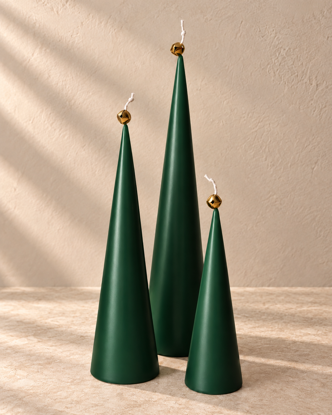 Forest green cone candle set with gold bells on warm beige stone; digitally styled color preview
