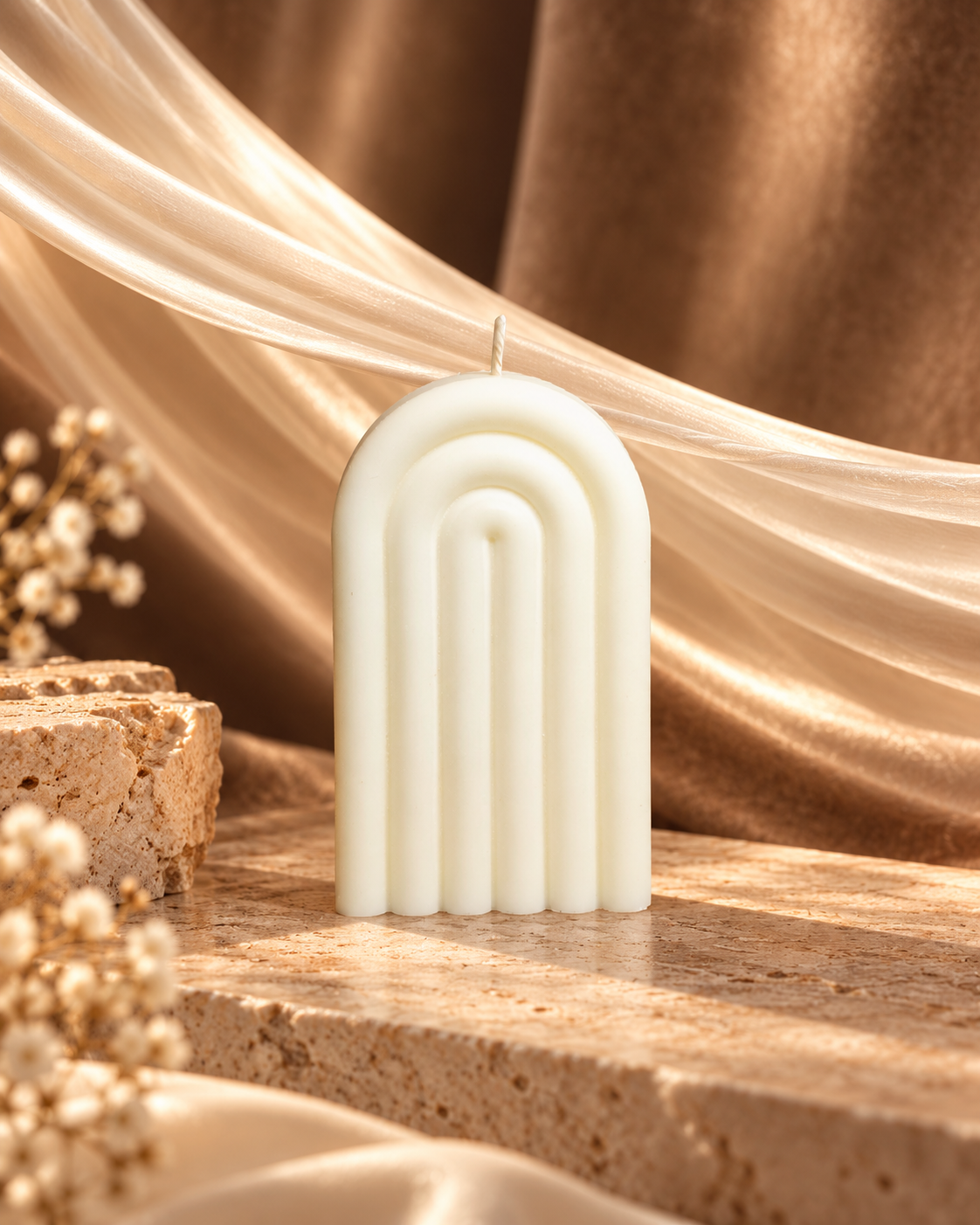 Ivory arch candle with rounded vertical ridges on warm stone beside draped fabric