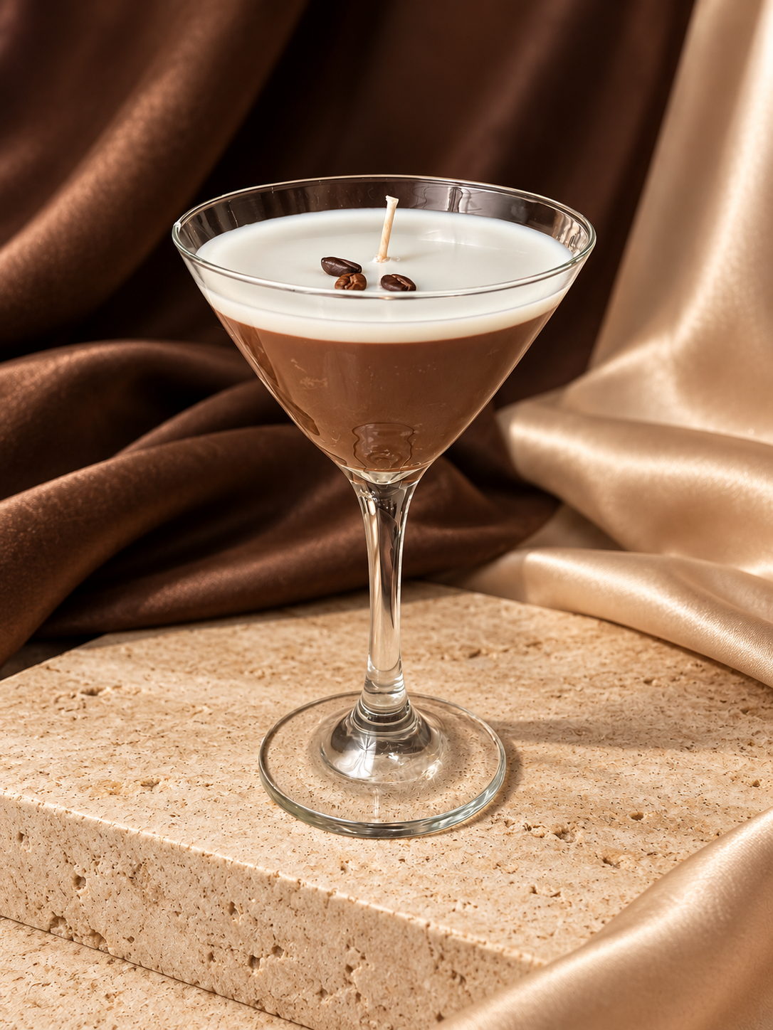 Espresso martini candle in a clear stemmed glass with brown and cream layers, styled on travertine with satin