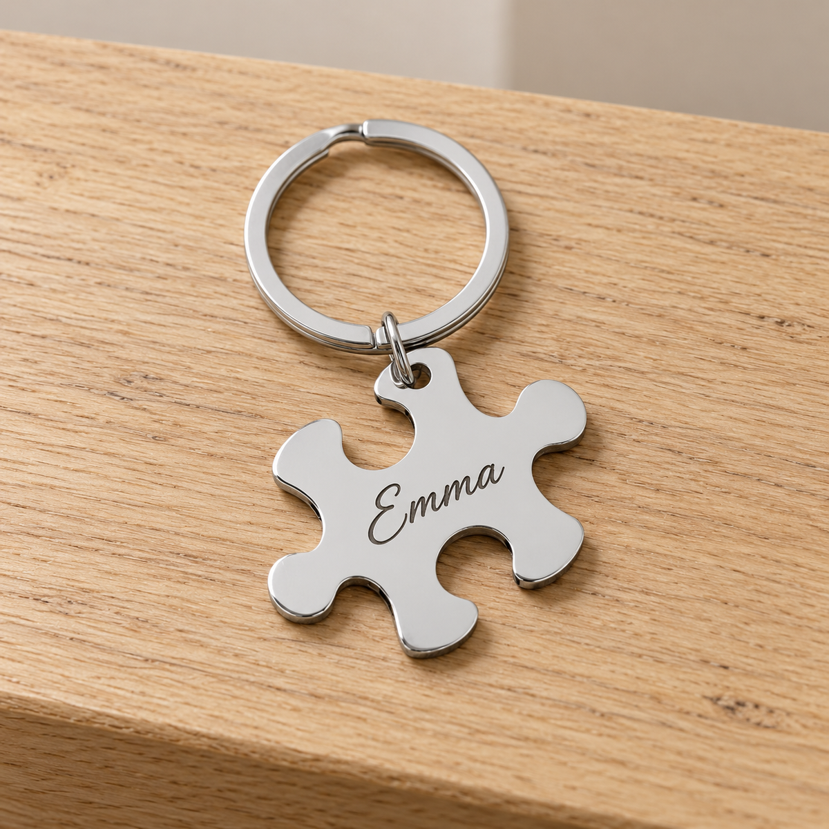 Silver puzzle piece keychain engraved Emma on a straight pale oak table; digital personalization preview